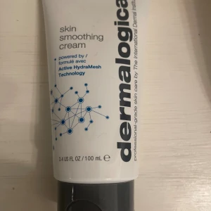 Dermalogica Skin Smoothing Cream 100ml - En vit tub med svart lock innehållande Dermalogica Skin Smoothing Cream, 100 ml. Ansiktskräm med Active HydraMesh Technology som återfuktar huden och skyddar mot miljöpåverkan. Tuben har blå och svarta detaljer och tydlig logotyp. Helt ny, nypriset är 950kr