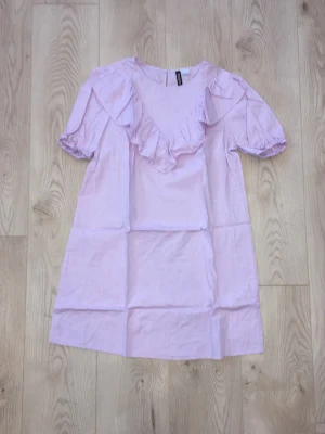 Ljuslila volangklänning med puffärm - Söt ljuslila klänning med volangdetaljer framtill och puffärmar. Klänningen har en rak, avslappnad passform. 