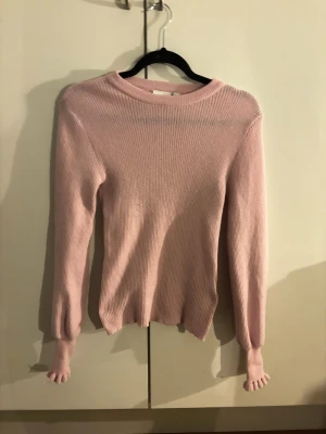 Ljusrosa ribbstickad tröja från VILA - Söt ljusrosa stickad tröja med ribbad struktur och rund hals. Tröjan har långa ärmar och smal passform, perfekt för lager på lager. Materialet ser mjukt och stretchigt ut, vilket gör den bekväm att bära till jeans eller kjol.