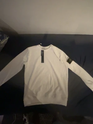 Vit sweatshirt från Stone Island - Snygg vit sweatshirt från Stone Island med klassisk rund hals och ikonisk logotyp-patch på vänster ärm. Tröjan har en stilren design och är tillverkad i mjukt material som passar perfekt till streetwear-looken.