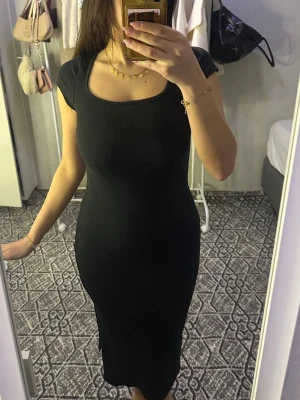 Svart ribbad klänning med slits - Snygg svart ribbad klänning med tight passform och korta ärmar. Klänningen har en rundad urringning och en slits på sidan som ger en extra detalj. Perfekt för dig som gillar en stilren och enkel look.