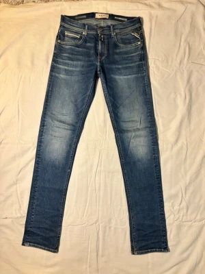 Blå straight fit jeans från Replay - Snygga blå straight fit jeans från Replay/grover/ med klassisk femficksdesign och slitna detaljer på låren och knäna. Jeansen har dragkedjegylf, kontrastsömmar och läderpatch med logga bak i midjan. Perfekta för en trendig och avslappnad stil.