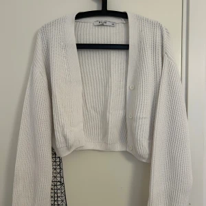 Vit kofta från NA-KD - Vit kofta med ribbad stickning och långa ärmar från NA-KD i storlek XXS. Koftan har v-ringad hals och tre knappar framtill. 