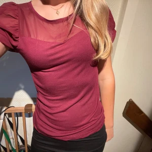 Vinröd topp med puffärm och mesh - Säljer en vinröd topp med kort puffärm och transparent mesh upptill. Toppen har rund halsringning och figurnära passform. Ärmarna är lätt rynkade och ger en trendig look. Perfekt för dig som gillar detaljer och en snygg siluett.