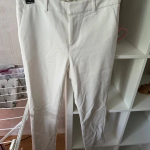 Vita kostymbyxor chinos från LC Waikiki strl: 38 - Snygga vita kostymbyxor från LC Waikiki med raka ben och diskreta bakfickor. Byxorna har hällor för bälte och är tillverkade i ett mjukt bomullsmaterial. Perfekta för en clean och fräsch look.