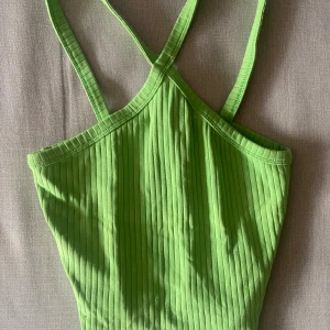 Ribbad grön linnetopp med korsade band - Snygg ribbad linnetopp i klargrönt med smala axelband som korsas i ryggen. Toppen är ärmlös och har en tight passform, perfekt för varma dagar eller lager på lager. Materialet är mjukt och stretchigt för extra komfort.