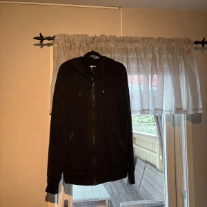Svart hoodie från C.P. Company L - Svart hoodie från C.P. Company i storlek L. Tröjan har dragkedja framtill, två fickor med dragkedja och justerbar huva med snörning. Tillverkad i mjuk bomull, perfekt för chill dagar. Klassisk och stilren design. PS lite stor i storlek passar Xl 