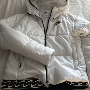 Vit Nike jacka  - Snygg vit pufferjacka från Nike med Therma-Fit-teknologi. Jackan har svart Nike-logga på bröstet, dragkedja framtill och huva. Har använts bara några gånger så väldigt bra skick ,köpt över 1000