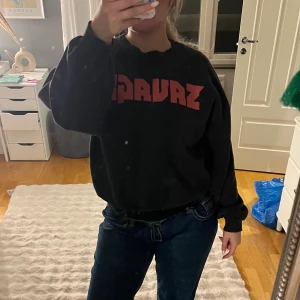 Svart sweatshirt från Gina Tricot - Svart sweatshirt från Gina Tricot med röd text framtill. Tröjan har en avslappnad passform, rund halsringning och långa ärmar med ribbade muddar. Perfekt för en chill och snygg vardagslook.