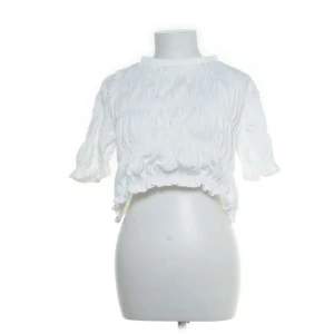 Vit blus från Daphnea Paris, M - Säljer en vit blus från Daphnea Paris i storlek M. Blusen är tillverkad i 100% bomull och har en croppad passform med korta ärmar och volangdetaljer vid ärmslut och nederkant. 