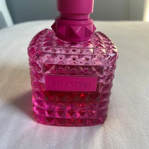 Valentino parfym i rosa glasflaska - Säljer en lyxig parfym från Valentino i en cool, fyrkantig glasflaska med nitar och mönstrad yta. Flaskan är intensivt rosa med matchande lock och etikett. Perfekt för dig som gillar statement-detaljer och snygg design. Det är en flaska med 100ml men det finns lite över 50ml kvar! Jag säljer pga att jag har tröttnat på doften! Skicka gärna prisförslag och ställ frågor vid funderingar!❣️nypris ca 1800kr!