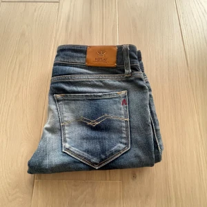Replay jeans i mörkblå med vintage - Snygga Replay jeans i mörkblå med vintage även med slitningar och klassiska kontrastsömmar. Modellen har raka ben och femficksdesign, med Replay-logga på bakfickan och läderpatch i midjan. Perfekta för dig som gillar en tidlös och stilren look.