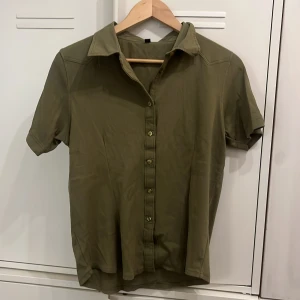 Olivgrön kortärmad skjorta Mascot - Säljer en olivgrön skjorta från Mascot med korta ärmar och klassisk krage. Skjortan har knappar hela vägen framtill och är gjord i ett mjukt bomullstyg. 