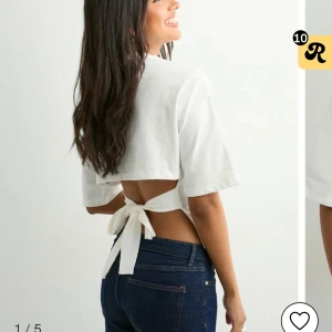 Vit croppad topp med knyt i ryggen - Säljer en vit croppad topp med korta ärmar och öppen rygg som knyts med en bred rosett. Toppen har en stilren look och är perfekt för varma dagar. Materialet känns lätt och luftigt.