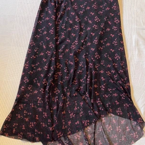 Svart blommig långkjol från Lindex - Supersnygg svart långkjol från Lindex med små rosa blommor över hela tyget. Kjolen har en lätt utsvängd form och resår i midjan för extra komfort. Perfekt för dig som gillar en romantisk och chill stil.