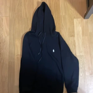 Polo Ralph Lauren hoodie - Svart hoodie från Polo Ralph Lauren med klassisk broderad logga på bröstet. Tröjan har huva med snörning och långa ärmar. Tillverkad i mjuk bomull för en skön känsla. Perfekt för dig som gillar stilren och enkel design.