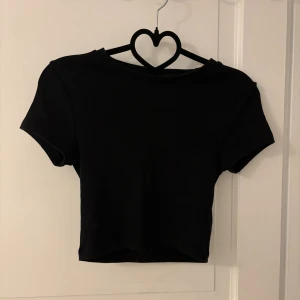 Svart croppad topp från Gina Tricot - En svart, enkel croppad topp från Gina Tricot i storlek S. Toppen har korta ärmar och rund halsringning. Gjord i mjukt material. 