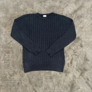 Mörkblå kabelstickad tröja John Henric - Kabelstickad mörkblå tröja från John Henric i klassisk modell. Tröjan har rund halsringning, ribbade muddar och är tillverkad i ett mjukt stickat material. Perfekt för lager-på-lager och snygg till jeans eller chinos.