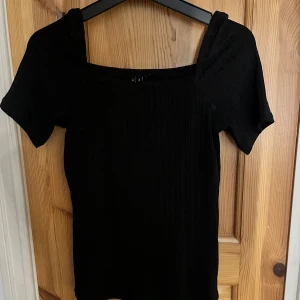 Svart ribbad topp med fyrkantig hals - Svart ribbad topp från vero moda med fyrkantig halsringning och korta ärmar. Materialet är stretchigt 
