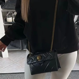 Svart quiltad axelväska Kurt Geiger - Säljer en svart quiltad axelväska från Kurt Geiger med guldfärgad kedja och ikonisk örndetalj på locket. Väskan är i skinn och har snygga sömmar i mönster. Dustbag kommer med 💗