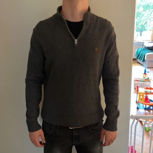 Mörkgrå half zip-tröja Abercrombie - Mörkgrå långärmad tröja från Abercrombie & Fitch med half zip och liten broderad logga på bröstet. Tillverkad i en mjuk blandning av bomull och merinoull. Ribbstickade muddar och krage ger en clean och stilren look. Modellen är 178 cm lång och väger 63 kg. Det är bara att höra av sig vid frågor och funderingar 😀
