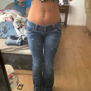 Blå bootcut jeans låg midja - Snygga blå jeans med bootcut och låg midja. Jeansen har klassiska fickor fram och bak, ljusa slitningar och sitter tajt över höfterna. Perfekta för dig som gillar en retro vibe och vill ha ett par jeans som framhäver figuren.