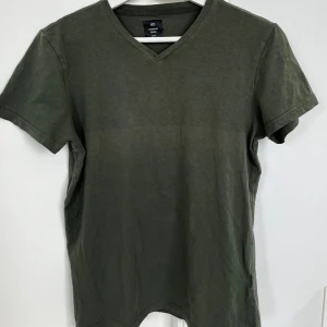 Olivgrön t-shirt med v-ringning 157 - En basic olivgrön t-shirt från 157 med v-ringad hals och korta ärmar. Tillverkad i mjuk bomull och har en clean, enkel look som passar till allt. Perfekt för dig som gillar stilrena plagg med skön passform.