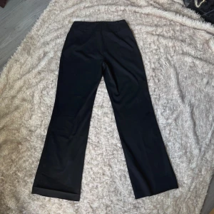 Svarta kostymbyxor med raka ben - Stilrena svarta kostymbyxor med raka, något vida ben. Byxorna har diskreta hällor för bälte och stängs med dold hake och knapp framtill. Materialet känns mjukt och följsamt.