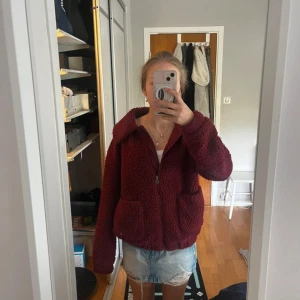 Vinröd teddyjacka med dragkedja - Vinröd teddyjacka från Only med dragkedja framtill och stora fickor. Jackan har en klassisk krage och är långärmad. Perfekt för dig som vill ha en varm och trendig look under  kalla dagar.