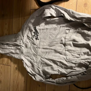 Grå vintage hoodie från Peak Performance - Grå hoodie från Peak Performance med svart broderad logga på bröstet. Tröjan har huva med snörning, som man ser på bild två är det två hål i ärmarna enkelt att laga men därav priset