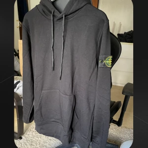 Svart hoodie från Stone Island Medium - Svart hoodie från Stone Island med klassisk patch på vänster ärm. Tröjan har huva med snörning, stor magficka och ribbade muddar. Tillverkad i mjuk bomull. Inga tecken på användning, har den i storlek medium.