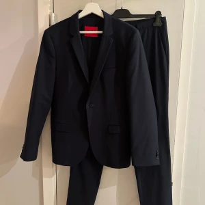 Mörkblå kostym från Hugo Boss - Säljer en stilren mörkblå kostym från Hugo Boss. Kavajen har klassisk passform med två knappar framtill, smala slag och fickor med lock. Nypris omkring 8000kr.