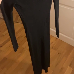 Svart ribbad långärmad klänning - Säljer en svart, ribbad långärmad klänning från new Yorker med hög hals. Klänningen är figurnära och har en enkel, stilren design som passar perfekt till sneakers eller boots. Materialet är stretchigt och bekvämt, vilket gör den lätt att bära hela dagen.