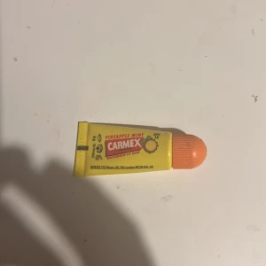 Carmex Pineapple Mint läppbalsam - Fuktgivande läppbalsam från Carmex i smaken Pineapple Mint. Kommer i en gul tub med orange skruvkork och har SPF 15. Perfekt för att hålla läpparna mjuka och skyddade mot solen.