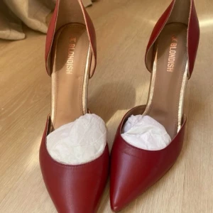 Röda pumps Blondish Ana Carla - Snygga röda pumps från Blondish, modell Ana Carla. Skorna har spetsig tå, hög klack och är tillverkade i skinn. De har en elegant och stilren design med öppen insida och klassisk siluett. Perfekta för att sticka ut med en djup röd färg och trendig look. Säljer pga för stora, endast använda en gång. Lägg ett bud❤️10 cm 