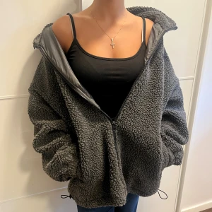 Grå teddyjacka från Dazy - Mysig och oversized grå teddyjacka från Dazy, Shein, med dragkedja framtill och hög krage. Jackan har en fluffig, fårullsliknande yta och två sidofickor. Perfekt för kalla dagar när du vill vara både varm och stilren.