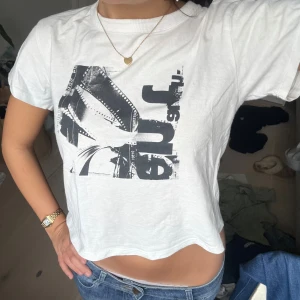 Vit croppad t-shirt med tryck - Säljer en vit croppad t-shirt med svart grafiskt tryck framtill. T-shirten har korta ärmar och en avslappnad passform.