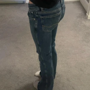 Lågmidjade bootcut jeans med slitna knän - Snygga blå lågmidjade bootcut jeans och slitna hål på båda knäna och snyggt knäppe från lager 157, köpta för 400 kr. Inte använda jättemycket men för långa så därav slitningar längst ner men inte något man tänker på.