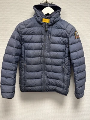 Mörkblå dunjacka från Parajumpers - Säljer en mörkblå dunjacka från Parajumpers med klassisk patch på ärmen och gul detalj vid halsen. Jackan har quiltad design, huva och dragkedja framtill samt praktiska fickor. Perfekt för kalla dagar och riktigt snygg till vardagslooken. 100% äkta. Skriv för frågor! Lite defekter på jackan och det är därför priset är lågt och det är enkelt att sy ihop!