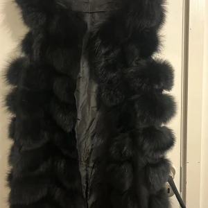 Svart fluffig pälsväst - Säljer en lång, svart pälsväst med riktigt päls. I god skick s-m, det är den långa modellen
