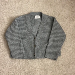Grå ribbad kofta från Zara - Mysig grå kofta från Zara i storlek 152. Koftan är ribbstickad med v-ringning och har tre knappar framtill. Långärmad och i en klassisk, enkel modell som passar perfekt till lager på lager under höst och vinter.