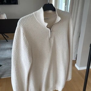 Beige stickad tröja John Henric half zip - Snygg beige stickad tröja från John Henric med strukturerat rutmönster och half zip-dragkedja vid kragen. Perfekt för lager-på-lager och passar till både jeans och chinos. Långärmad och i mjukt material som känns skönt mot huden.