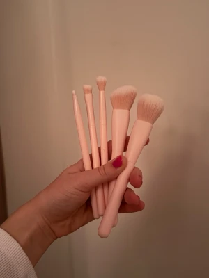 Rosa Sminkborstset    - Säljer ett set med fem sminkborstar i ljusrosa färg. Borstarna har mjuka syntetiska strån och olika former för både ansikte och ögon, perfekt för att applicera foundation, rouge och ögonskugga. Handtagen är i matchande rosa plast. Helt oanvända.