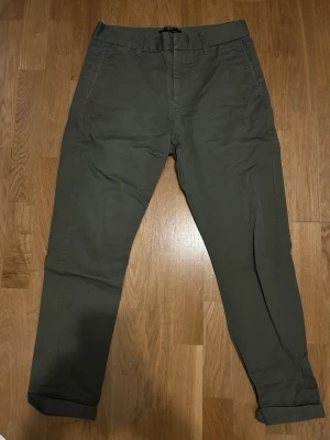 Mörkgröna chinos med tapered fit - Snygga mörkgröna chinos med tapered passform och klassiska sidfickor. Byxorna har bälteshällor och är tillverkade i ett mjukt bomullsmaterial som ger en skön känsla. Perfekta för en clean och avslappnad stil.