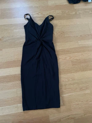 Svart klänning från H&M - Säljer en svart midiklänning från H&M med smala axelband och snygg twistad detalj framtill i midjan. Klänningen har en figurnära passform.