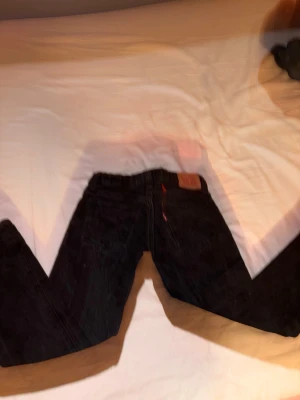 Levi's 501 svarta jeans - Säljer ett par klassiska svarta Levi's 501 jeans med raka ben och knappgylf. Jeansen har den ikoniska röda Levi's-lappen på bakfickan och patch i läder bak i midjan. Tillverkade i slitstarkt bomullstyg och har en tidlös look som funkar till allt.
