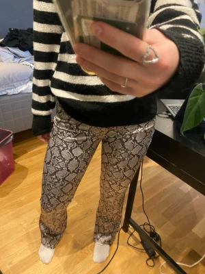Ormmönstrade bootcut byxor - Säljer ett par snygga byxor med ormmönster i svart och beige. Byxorna har bootcut-modell och sitter tajt upptill med utsvängda ben. Supercoola och sitter bekvämt!!