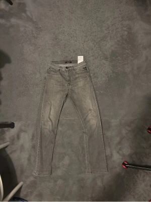Grå  jeans från Replay och blå  - Säljer ett par grå jeans från Replay med passform och klassisk femficksdesign. Jeansen har dragkedja och knapp i midjan samt diskreta slitningar för en cool look. Perfekta för dig som gillar stilrena och moderna jeans.