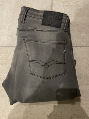 Replay grå jeans slim fit W30 L34 - Säljer ett par gråa Replay jeans i slim fit med klassisk femficksdesign och snygga detaljer på bakfickorna. Jeansen har normal midja och raka ben, tillverkade i mjukt och stretchigt bomullsmaterial för skön passform.