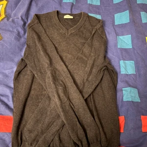 Mörkgrå v-ringad cardigan John Henric - Snygg mörkgrå v-ringad cardigan från John Henric i storlek S. Cardiganen är stickad och har långa ärmar med ribbade muddar vid hals, ärmslut och nederkant. Perfekt för dig som gillar klassisk och enkel stil med en modern touch.